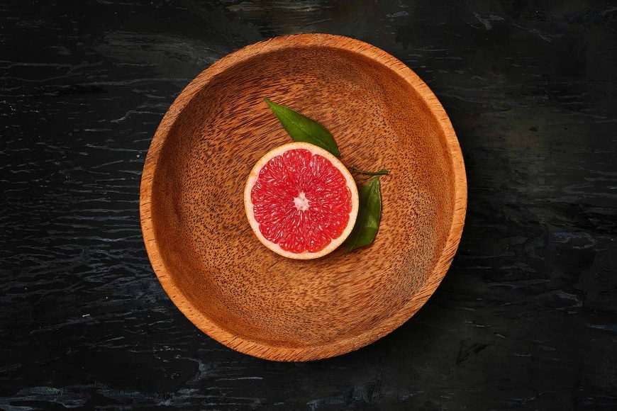 grapefruit-citrus-fruit-halves-on-wooden-plate-PHCQJD7